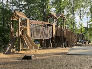 Wooden playground structure with slides and climbing features in a sunny park.