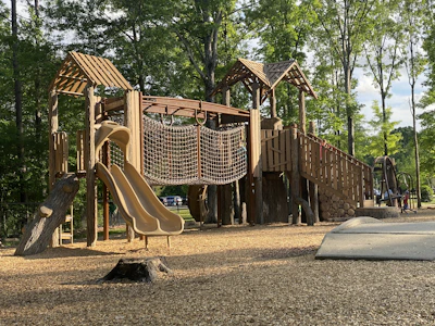 A beautifully crafted wooden playground structure in a sunny park setting.
