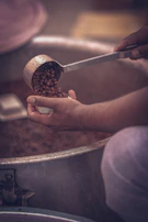 Hand pouring fitswad chole masala over chickpeas simmering in a traditional Indian pot.