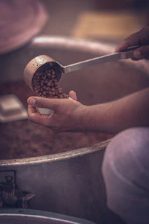 Hand pouring fitswad chole masala over chickpeas simmering in a traditional Indian pot.