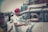 A person wearing a red turban is handing metal containers to another person seated in a white car. The scene seems to be outdoors with a blurred background that includes another person and a vehicle.