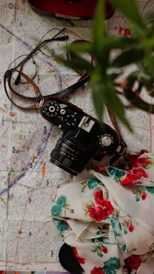 A mint green travel camera perched on a wooden table beside a map and sunglasses.