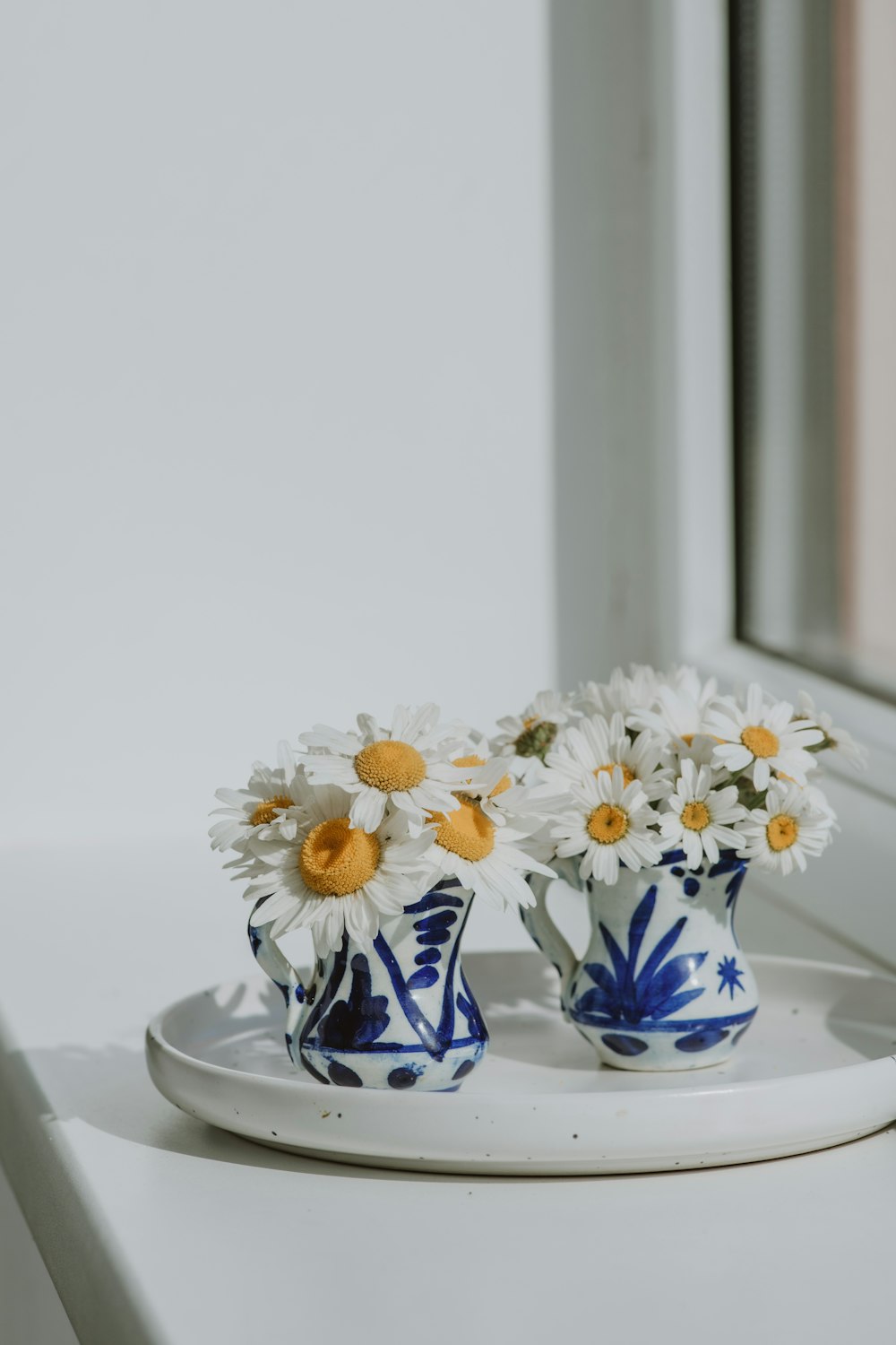 two blue and white vases with daisies on a plate