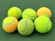 Variety of tennis balls in different vibrant colors displayed on a wooden surface.