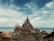 An intricately designed wooden temple sits majestically by the sea, its elaborate spires and carvings reaching towards the sky. The structure is surrounded by lush greenery, and the ocean stretches out behind it, meeting a partly cloudy sky.
