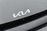 A car hood appears with water droplets scattered across it, featuring a silver logo in the center.