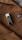 A metallic accessory with a sleek, reflective surface is clipped onto a brown fabric, likely part of a coat. There is also a black button with a glossy finish visible on the fabric.