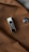 A metallic accessory with a sleek, reflective surface is clipped onto a brown fabric, likely part of a coat. There is also a black button with a glossy finish visible on the fabric.