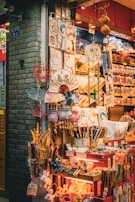 A vibrant market stall displays an array of traditional Asian items, including decorative fans, umbrellas, plates, and small toys. The stall is brightly lit and colorful, with intricate patterns and designs on many of the products.