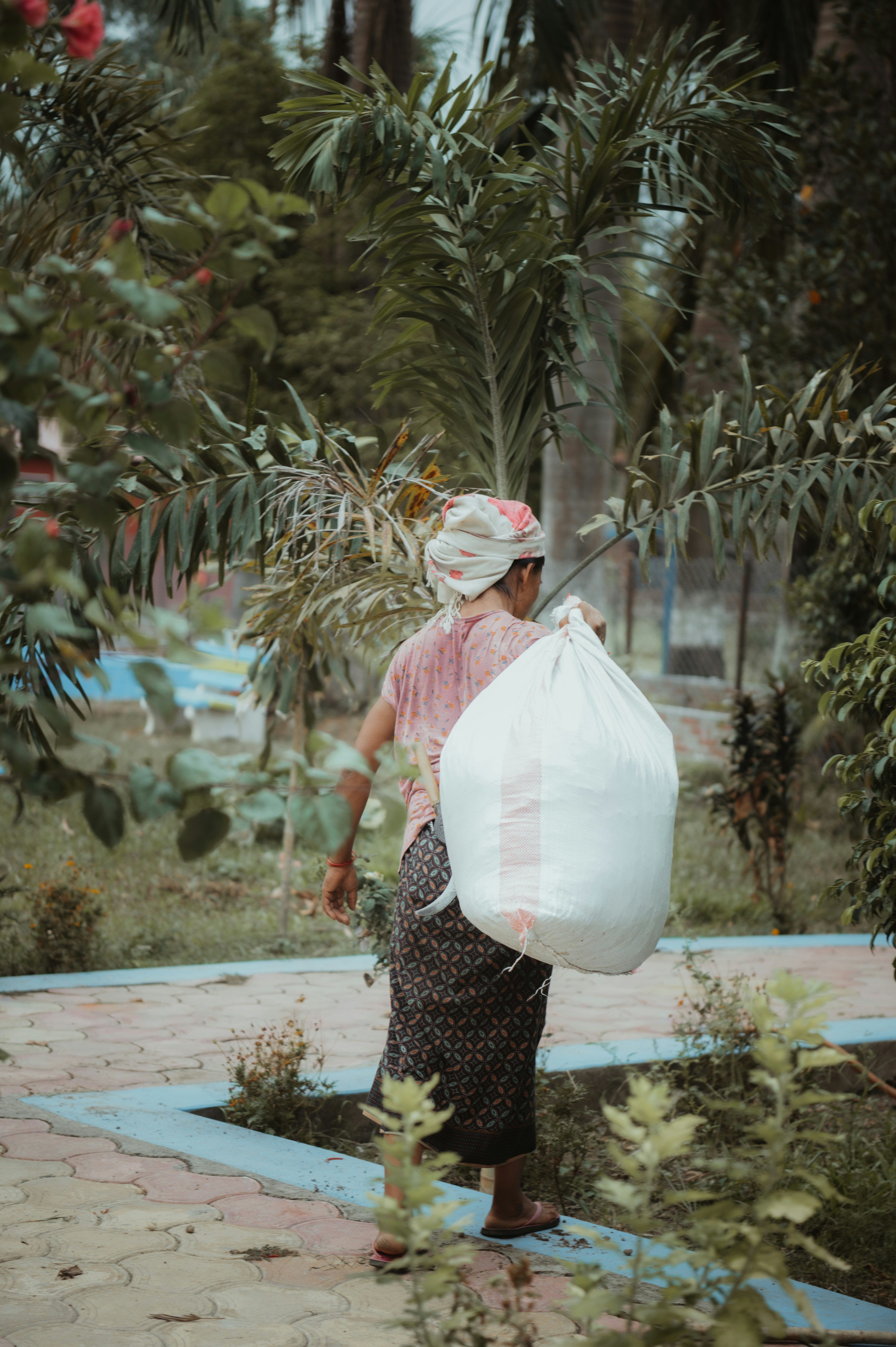 a woman carrying a large bag through a garden