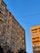 Two residential buildings with multiple stories are captured against a backdrop of clear blue sky. The walls have a textured appearance, and each building has numerous windows. Power lines stretch across the scene, and a few trees are visible at the bottom.