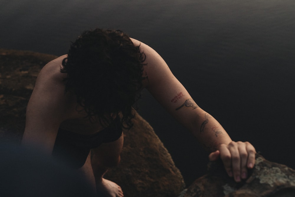 a woman with a tattoo on her arm leaning on a rock