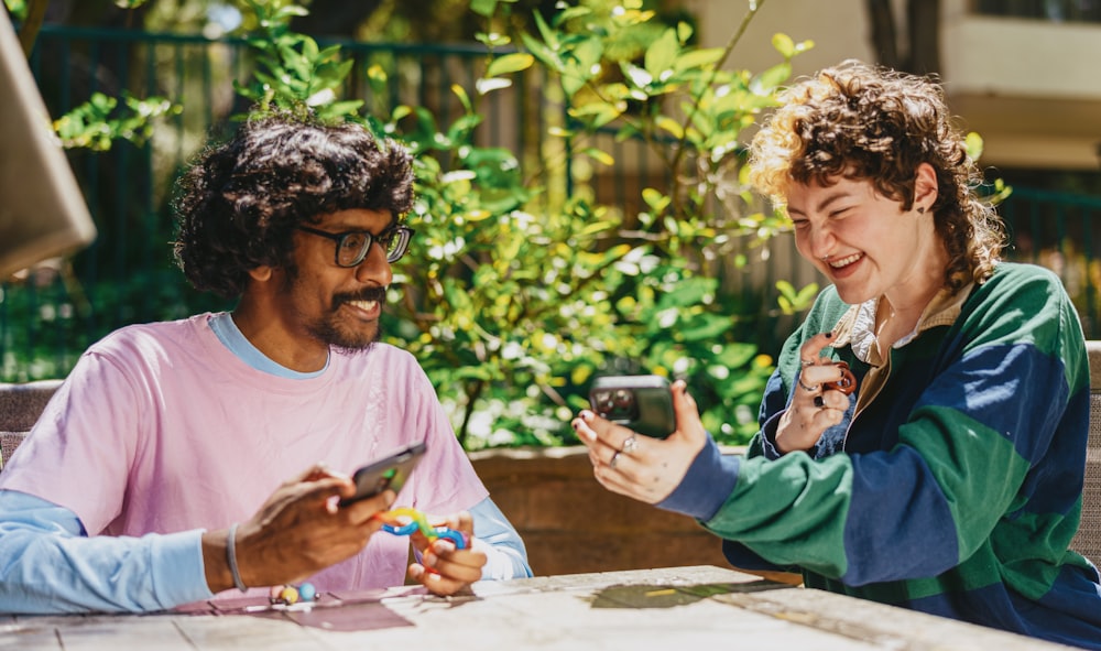 Dois amigos autistas sentados do lado de fora usando brinquedos stim e rindo de seus telefones