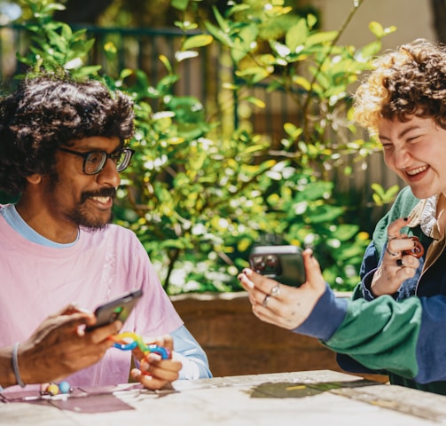 Two autistic friends sitting outside using stim toys and laughing at their phones