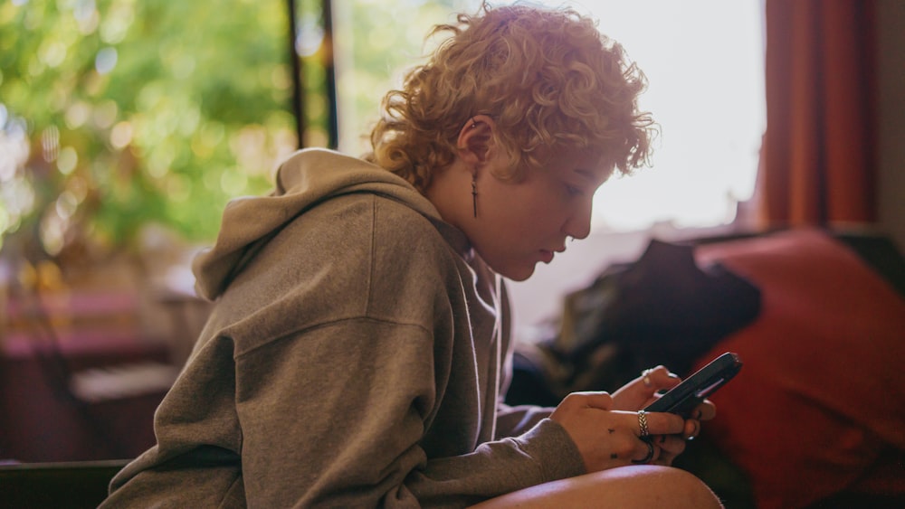 Retrato de una persona autista no binaria usando su teléfono móvil en interiores