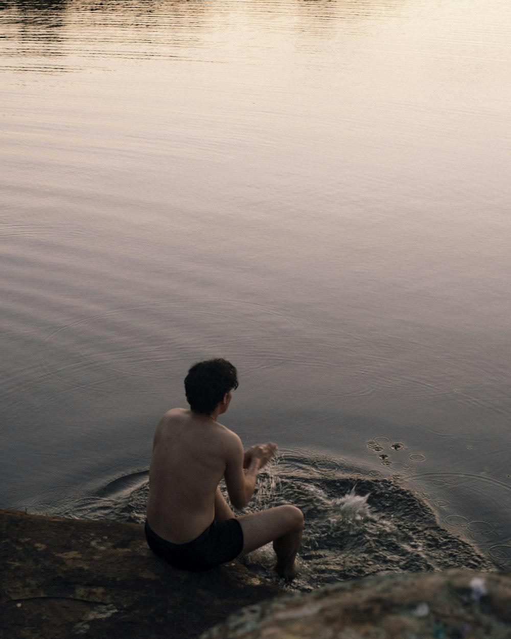 a man sitting on the edge of a body of water