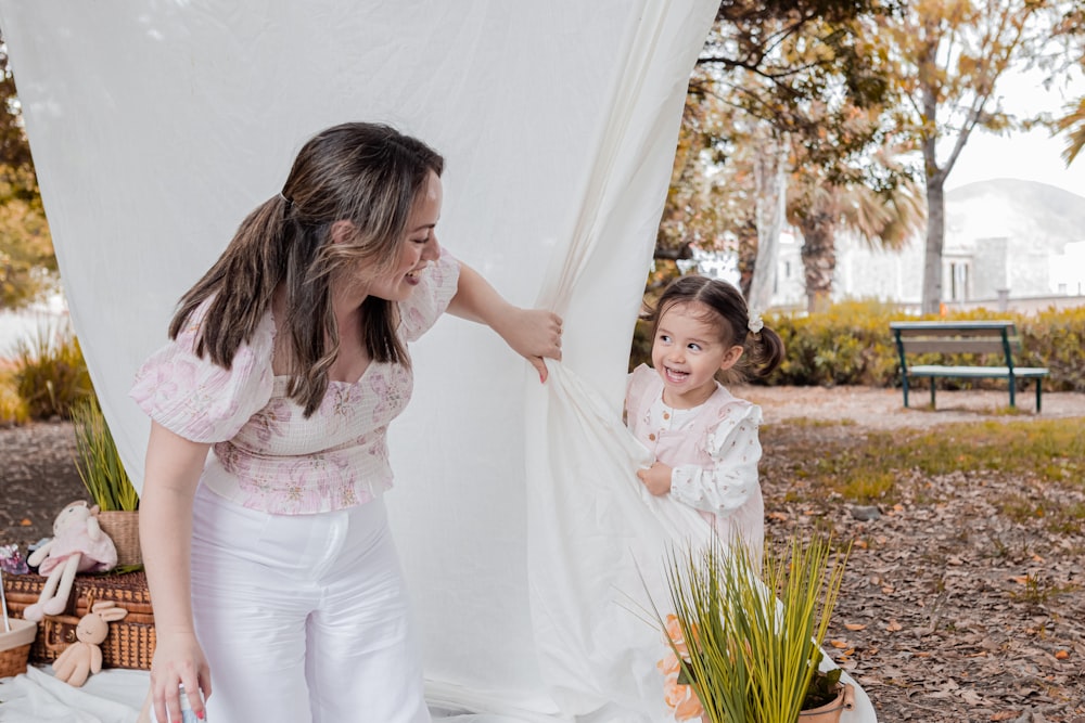 a woman and a little girl standing in front of a white curtain