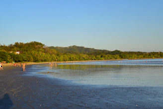 Tourists admiring a serene Bali beach at sunset with calm waves and golden sky.