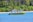 A yellow boat labeled 'SAMARA ADVENTURES' is floating on a blue body of water near a tropical shoreline lined with dense green palm trees and other vegetation.