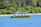 A yellow boat labeled 'SAMARA ADVENTURES' is floating on a blue body of water near a tropical shoreline lined with dense green palm trees and other vegetation.