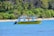 A yellow boat labeled 'SAMARA ADVENTURES' is floating on a blue body of water near a tropical shoreline lined with dense green palm trees and other vegetation.