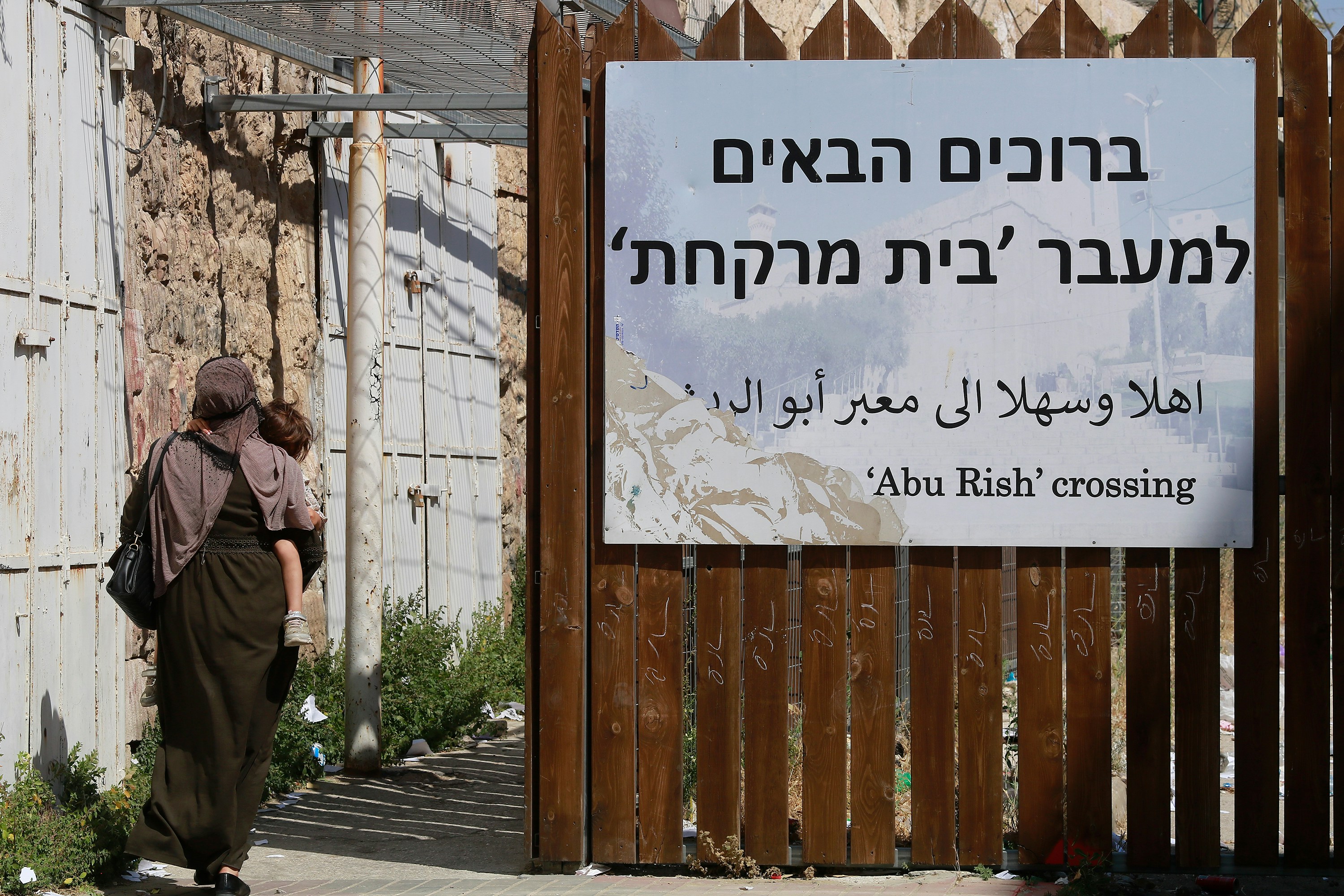 a woman walking past a wooden fence with a sign on it
