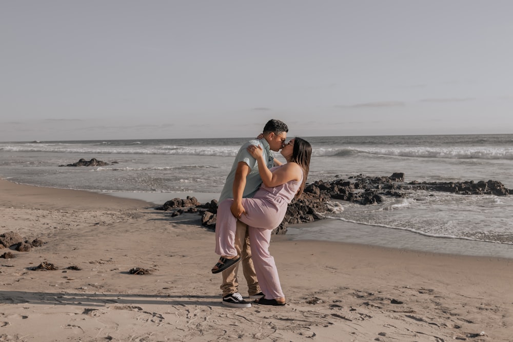 a man and woman standing on a beach next to the ocean