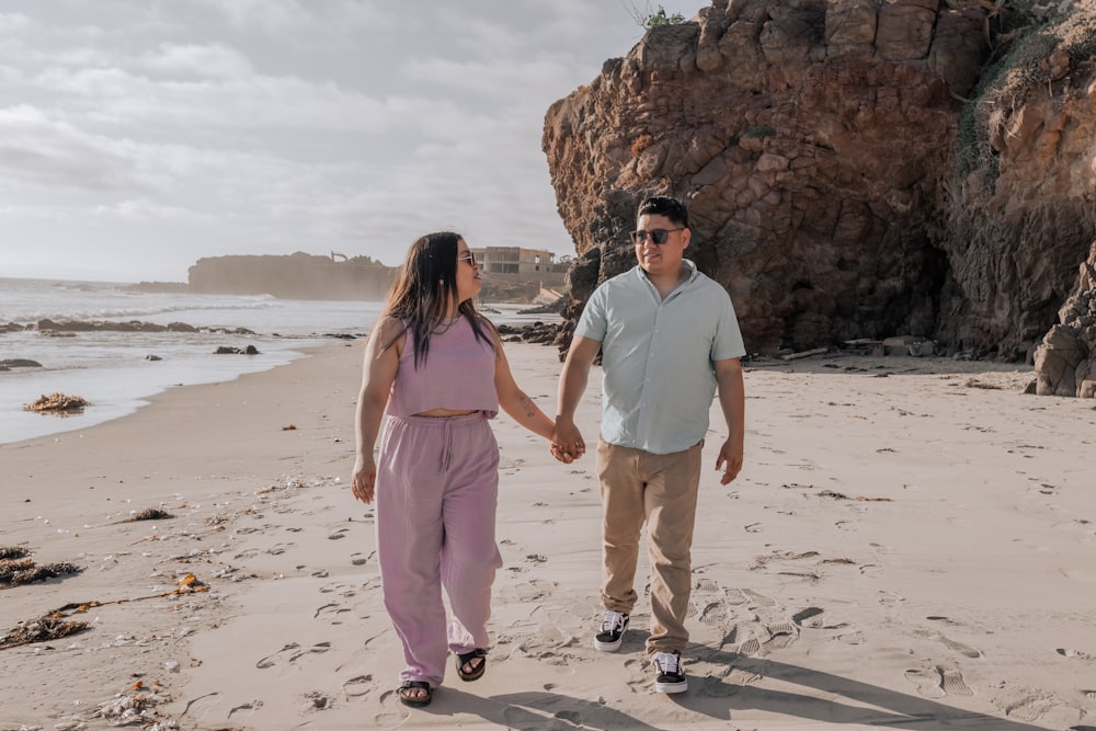 a man and woman walking on a beach holding hands