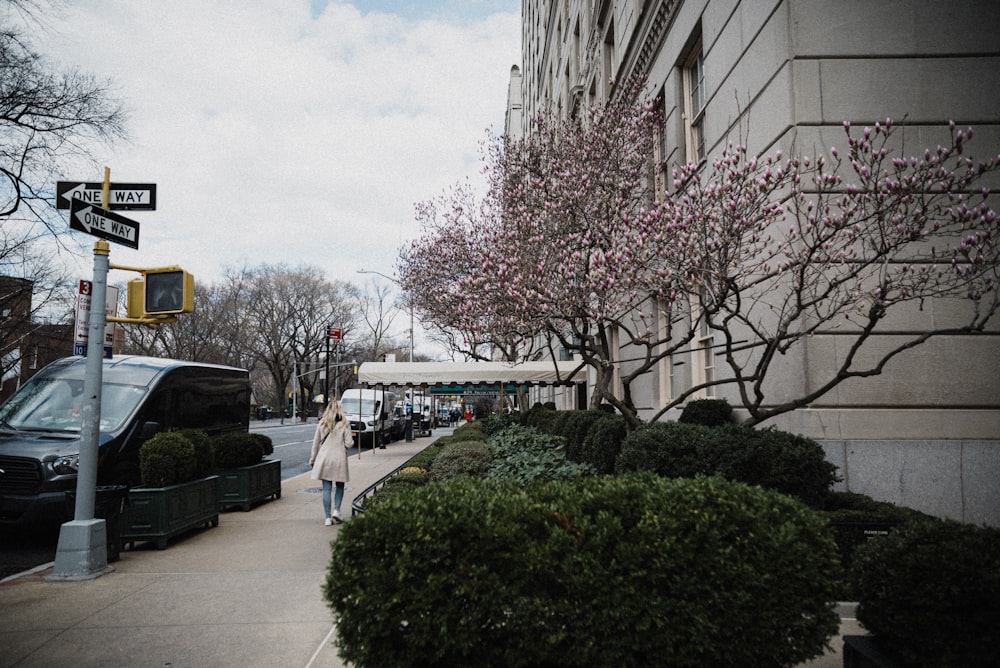 a woman walking down a sidewalk next to a tree