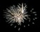 An elaborate display of fireworks with bright, white and gold sparks radiating in different directions against a dark sky.