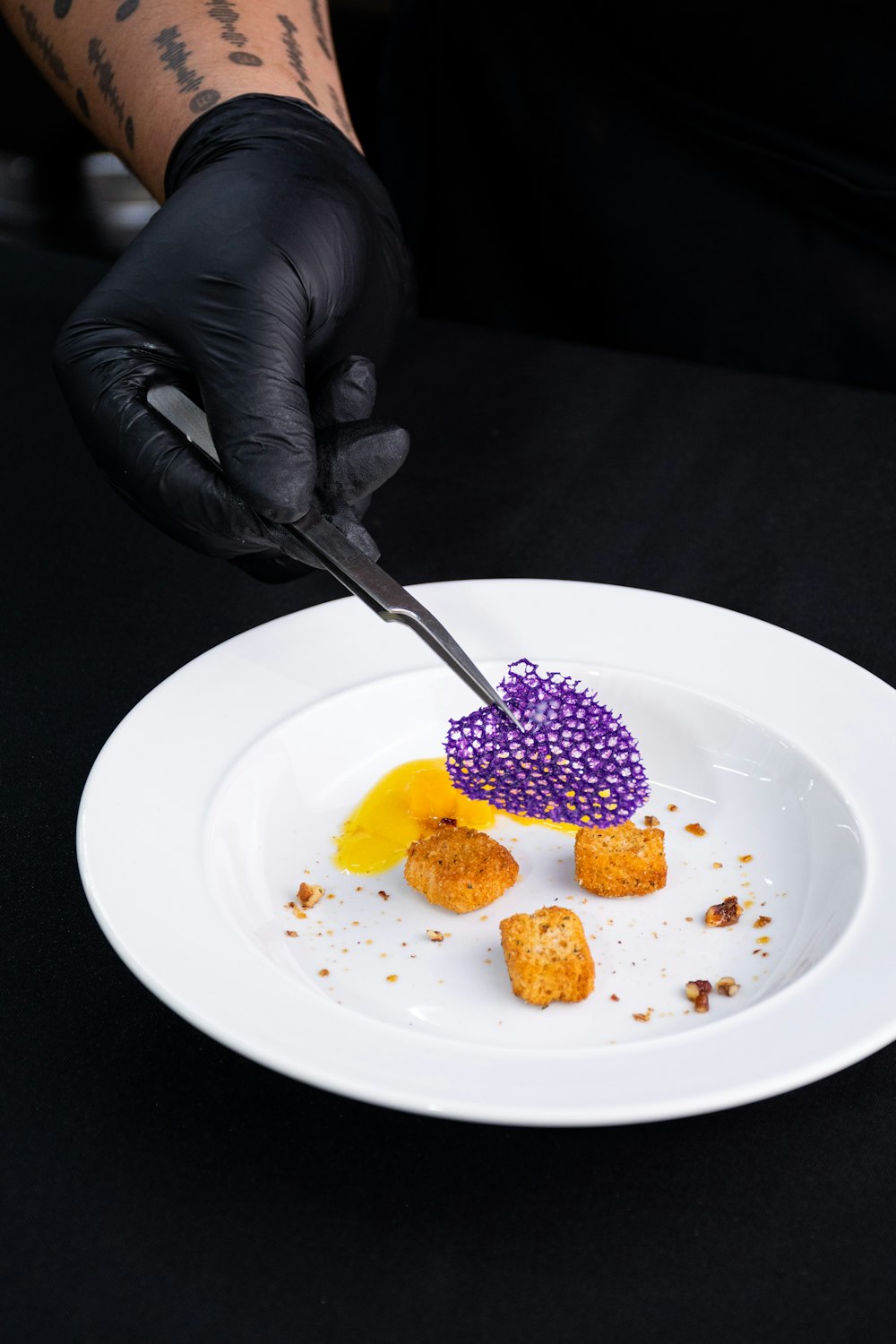 a person in black gloves is cutting a piece of food on a white plate