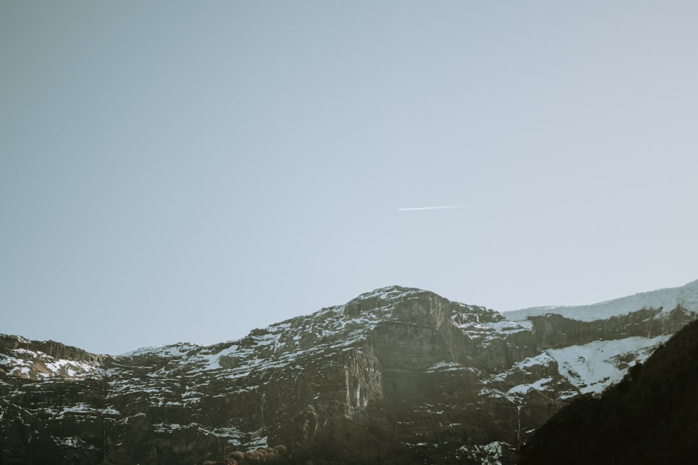 a view of a mountain with a plane flying in the sky