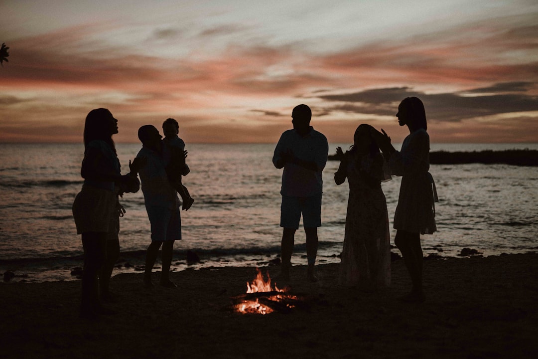 a group of people standing around a fire on a beach,