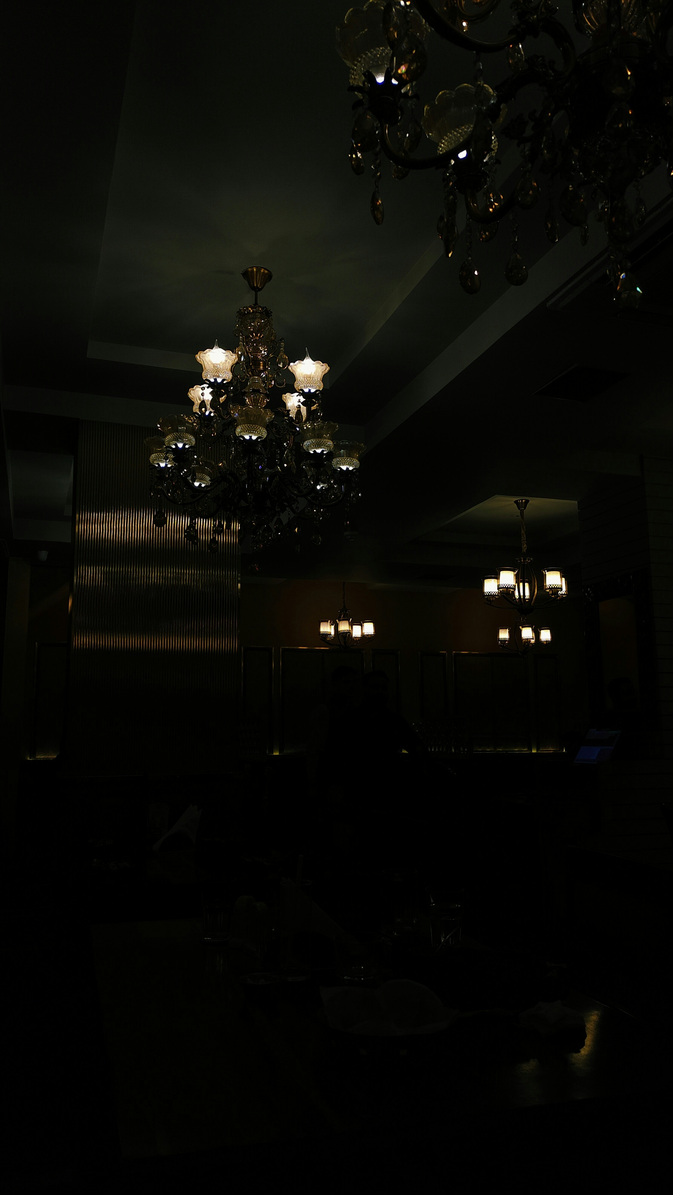 Upscale restaurant dining room with dim warm lighting, dark wood furniture, moody atmospheric ambiance