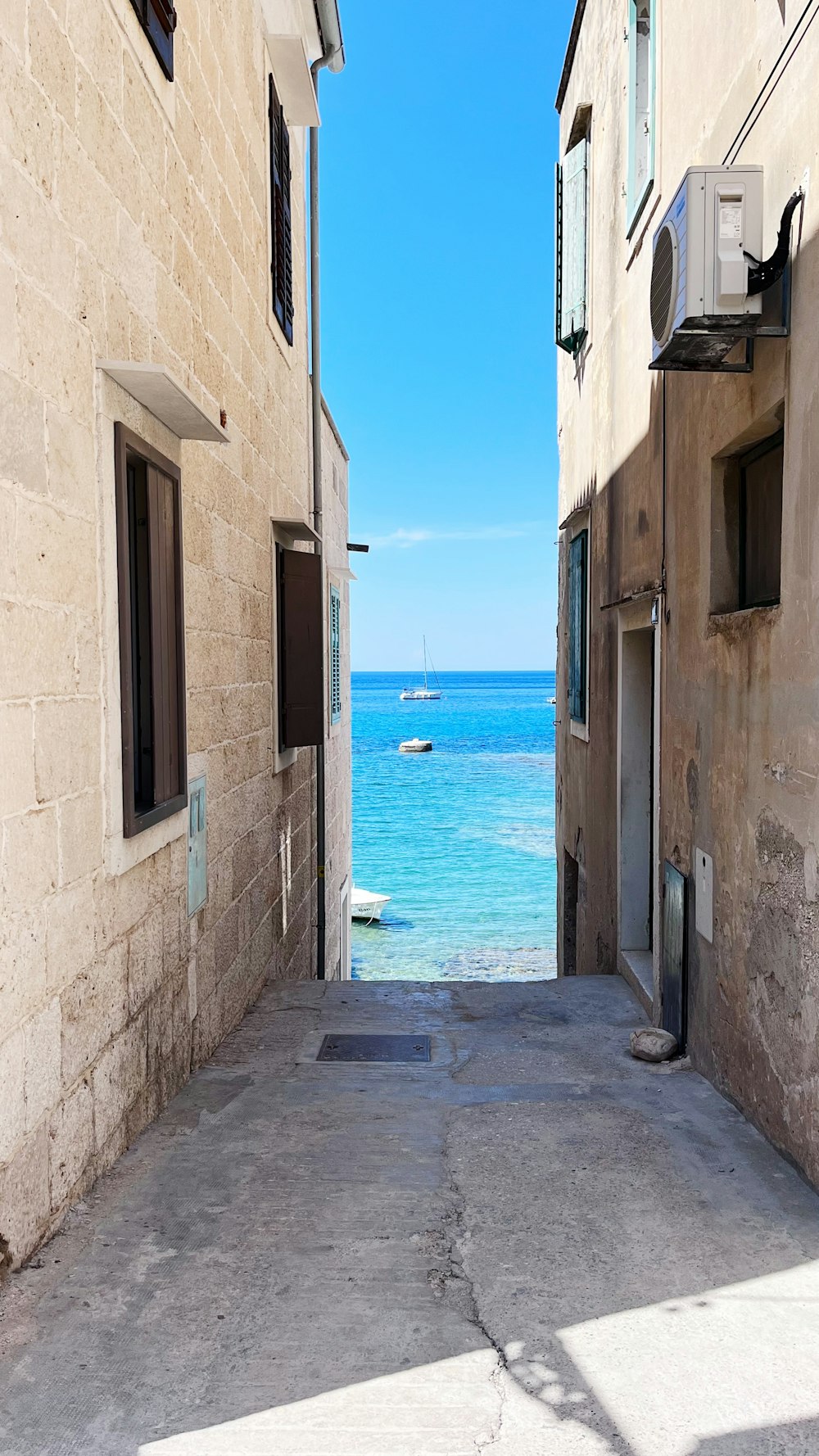 a narrow alley leading to a beach with a boat in the water