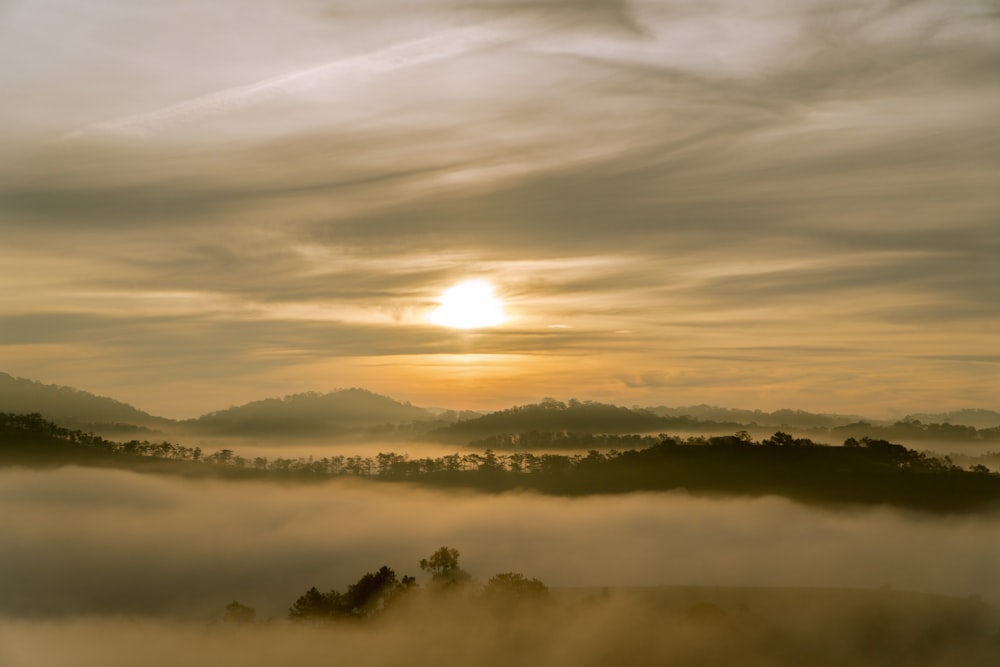 the sun is setting over a foggy valley