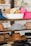 A variety of hats displayed on wooden shelves, including rolled-up hats in a white basket, a striped black and white hat, tan and brown hats, and a pink hat. The background is slightly blurred, giving a focus on the hats.