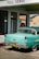 A vintage teal car with a black and yellow California license plate is parked under a 'FULL SERVE' gas station awning. There is an American flag sticker on the rear bumper. The building has white walls with green trim and a red tiled roof. A retro 'Drink Coca-Cola' sign and 'RESTROOM' sign are visible through the glass window.