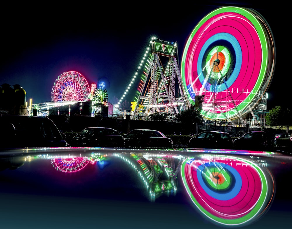 a ferris wheel lit up at night with a ferris wheel in the background