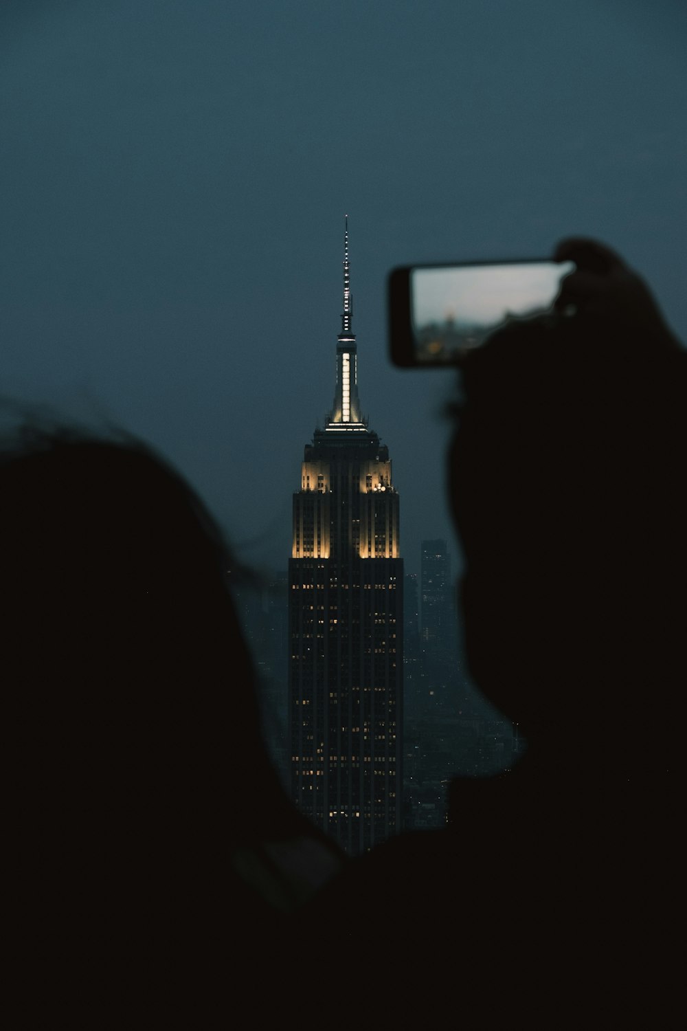 a person taking a picture of the empire building at night