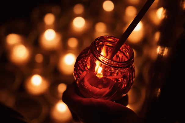 Hand holding a small vial of fragrance oil against a backdrop of warm, glowing candles.