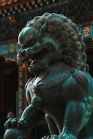 A detailed bronze statue of a mythical lion-like creature with elaborate curls in its mane and ornate decorations adorning its body. The background features traditional architecture with intricate patterns and Chinese characters.
