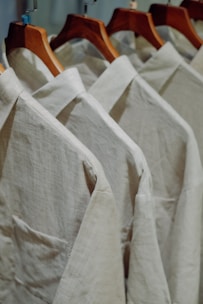Close-up of a flowing silk blouse in warm beige, draped gently on a hanger against a minimalist backdrop.