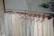 A row of light-colored sleeveless tops and pants hang neatly on wooden hangers. The clothing is displayed on a metal rack in a minimalist setting with a calm, natural background.