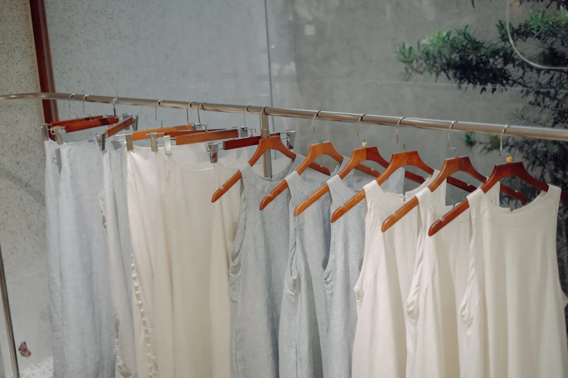 A neatly arranged display of minimalist men's shirts in neutral tones on wooden hangers.