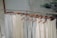 A row of light-colored sleeveless tops and pants hang neatly on wooden hangers. The clothing is displayed on a metal rack in a minimalist setting with a calm, natural background.