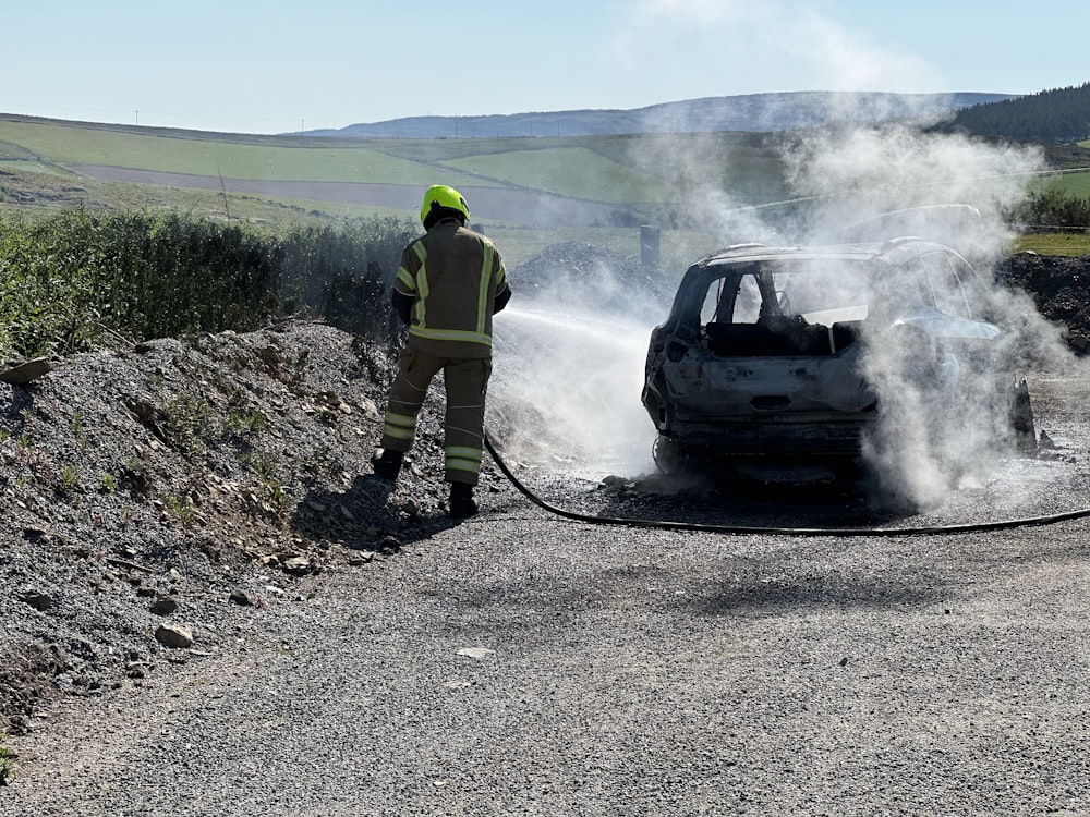 a man in a yellow safety jacket is next to a car that is on fire