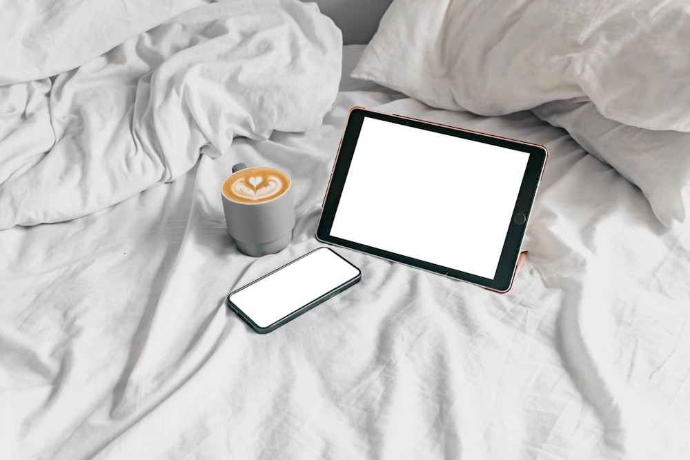 a tablet and a cup of coffee on a bed