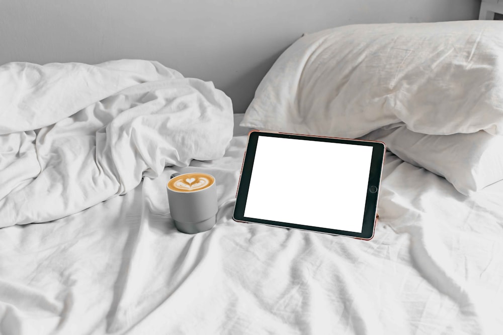 a cup of coffee and a tablet on a bed