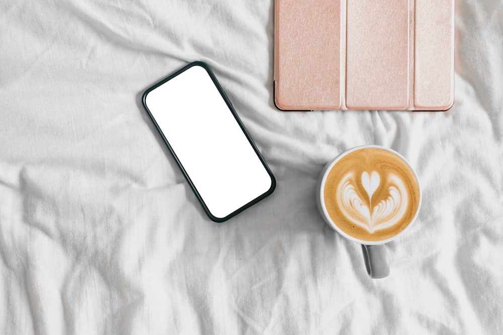 a cup of coffee and a cell phone on a bed